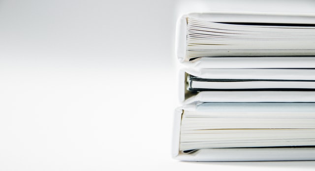 Image of a stack of white binders with documents, representing how court reporting technology can enhance traditional record-keeping methods and the need for services provided by Coash & Coash Court Reporting and Video.